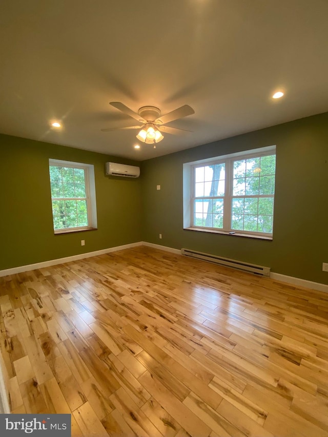 unfurnished room featuring a baseboard heating unit, ceiling fan, a wall unit AC, and light hardwood / wood-style floors