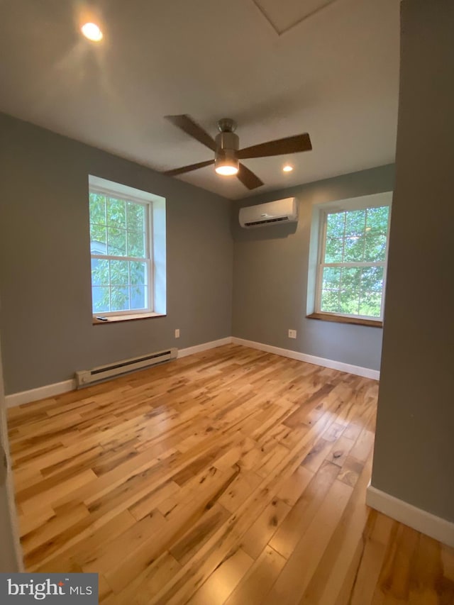 spare room featuring a healthy amount of sunlight, ceiling fan, a baseboard heating unit, an AC wall unit, and light hardwood / wood-style floors