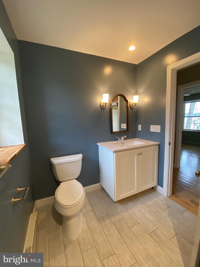 bathroom with a baseboard heating unit, wood-type flooring, toilet, and vanity