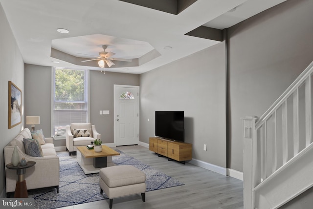 living room with ceiling fan, a raised ceiling, and light hardwood / wood-style floors