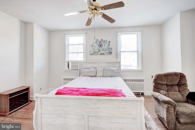 bedroom featuring baseboards, cooling unit, light wood-style flooring, and radiator