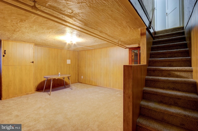 finished basement with light carpet, wood walls, and stairs