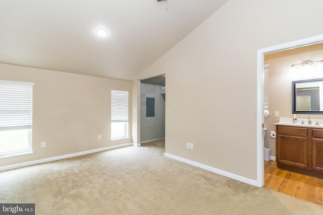 unfurnished bedroom featuring multiple windows, vaulted ceiling, connected bathroom, and light hardwood / wood-style flooring