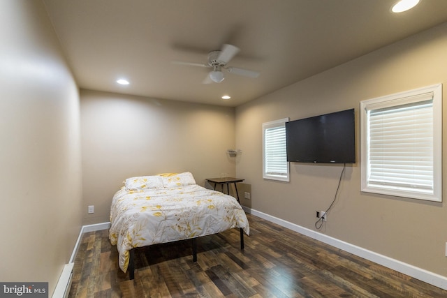 bedroom featuring a baseboard heating unit, multiple windows, dark hardwood / wood-style flooring, and ceiling fan