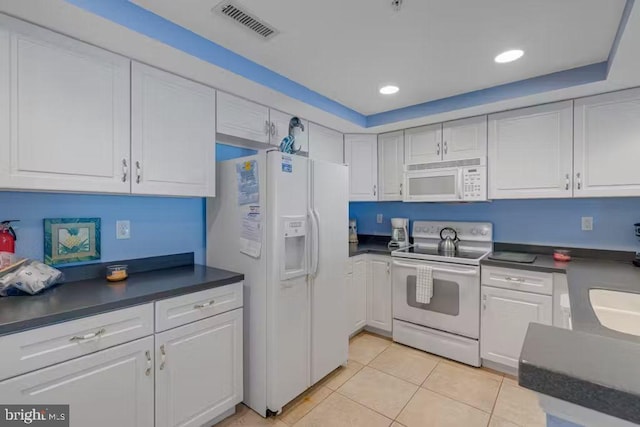 kitchen featuring a raised ceiling, white appliances, light tile patterned floors, and white cabinets