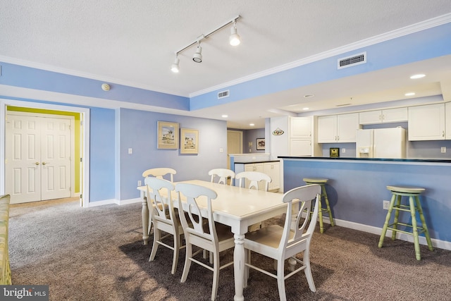 carpeted dining space with rail lighting, a textured ceiling, and crown molding