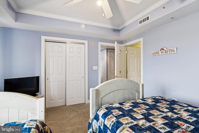 carpeted bedroom with ornamental molding, ceiling fan, a tray ceiling, and a closet