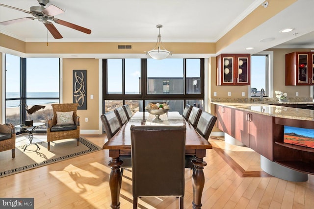 dining space with crown molding, a water view, a wealth of natural light, and light wood-type flooring