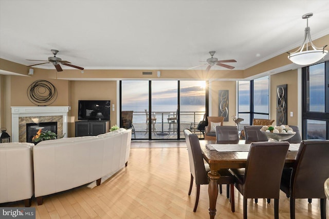 dining area featuring ceiling fan, ornamental molding, a fireplace, and light hardwood / wood-style flooring