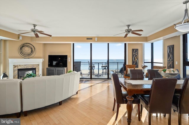 dining space featuring ceiling fan, ornamental molding, a premium fireplace, and light wood-type flooring