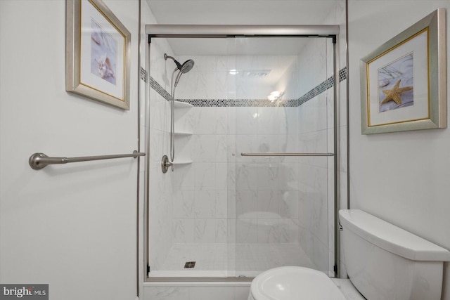 bathroom featuring a shower with shower door and toilet