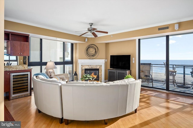 living room featuring wine cooler, a healthy amount of sunlight, crown molding, and a high end fireplace