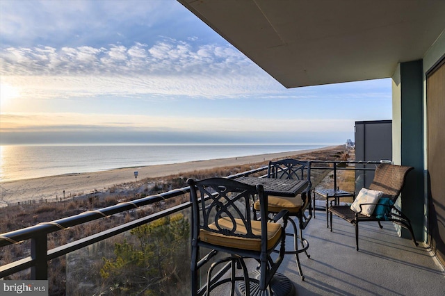 balcony at dusk featuring a view of the beach and a water view