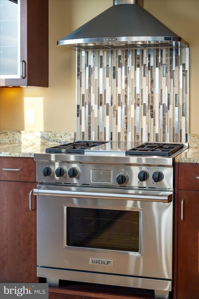 kitchen with light stone counters, ventilation hood, and premium stove