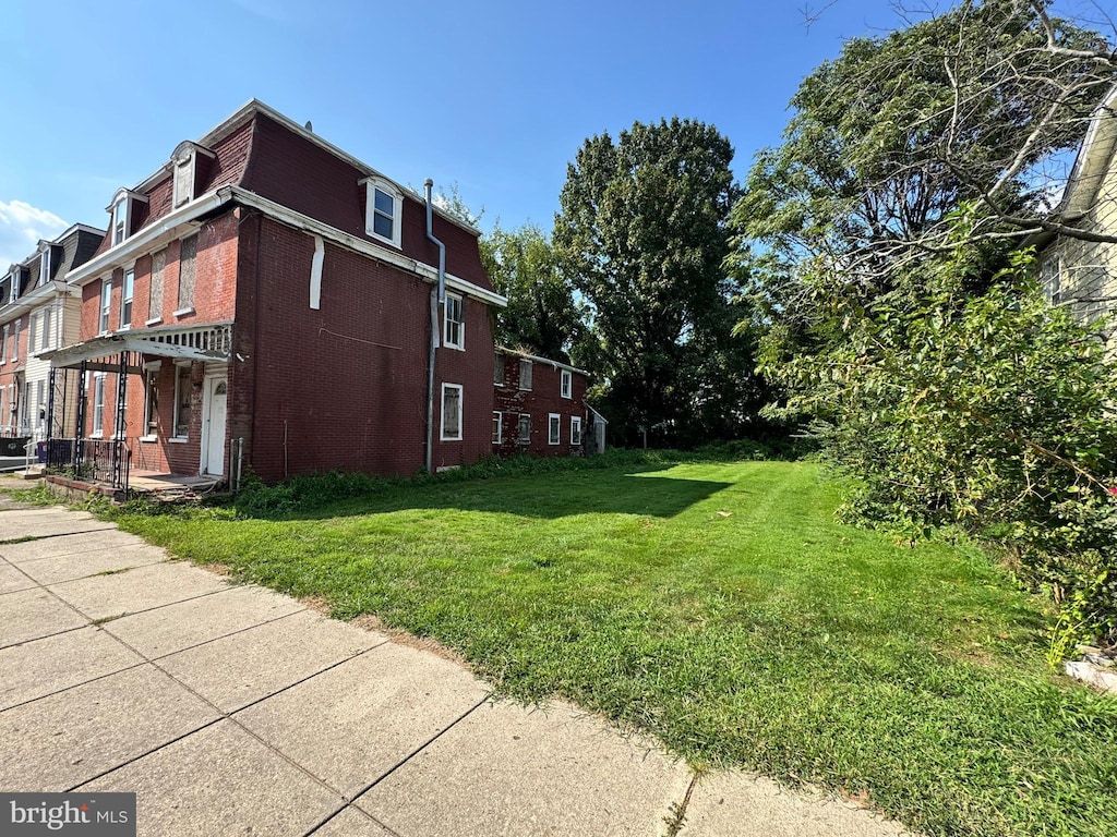 view of property exterior featuring brick siding, a lawn, and mansard roof