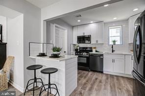 kitchen featuring a kitchen breakfast bar, light wood-type flooring, stainless steel appliances, sink, and white cabinets