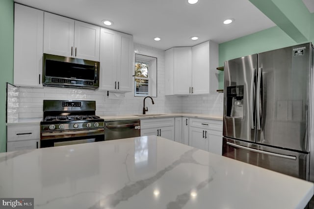 kitchen with light stone countertops, appliances with stainless steel finishes, backsplash, sink, and white cabinets