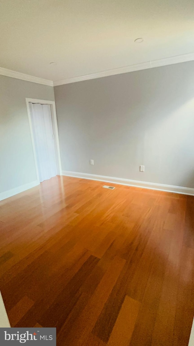 empty room with hardwood / wood-style floors and crown molding