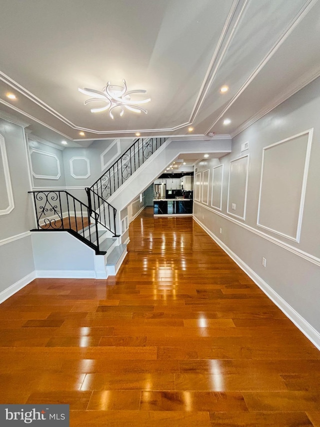 interior space with a decorative wall, wood finished floors, baseboards, ornamental molding, and stairway