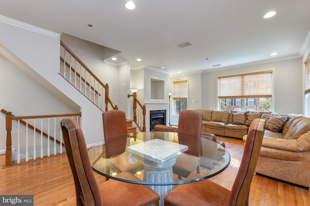 dining area featuring light wood-style flooring, recessed lighting, visible vents, a glass covered fireplace, and crown molding