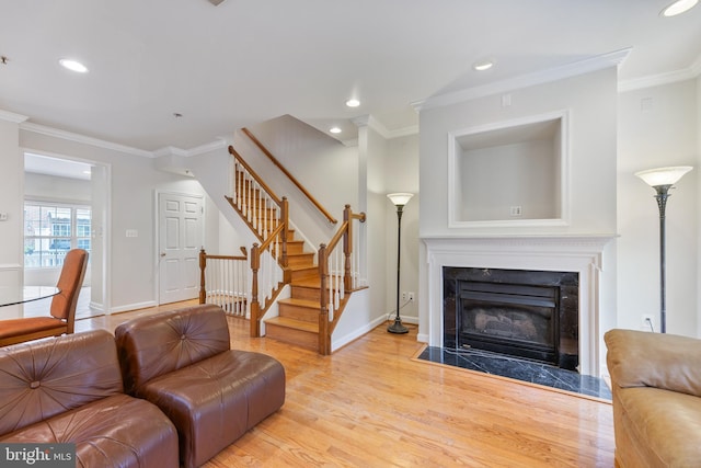 living room featuring light wood-type flooring, a premium fireplace, stairway, and crown molding