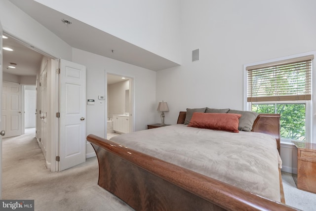 bedroom featuring a high ceiling, ensuite bath, visible vents, and light colored carpet