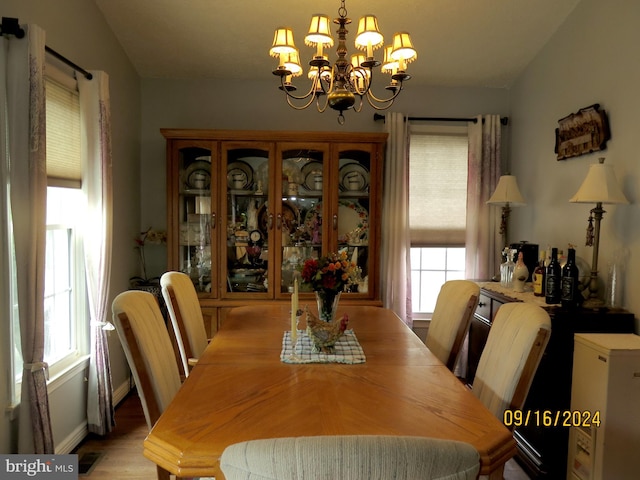 dining room featuring lofted ceiling, a healthy amount of sunlight, light wood-type flooring, and an inviting chandelier