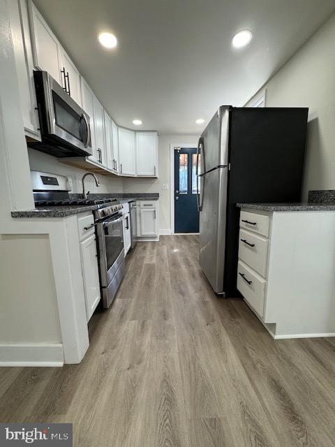 kitchen with dark countertops, light wood finished floors, white cabinetry, and stainless steel appliances