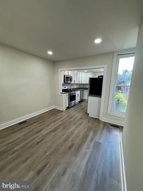 kitchen with stainless steel appliances, dark wood-type flooring, white cabinetry, baseboards, and dark countertops