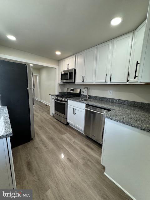 kitchen featuring recessed lighting, stainless steel appliances, a sink, white cabinets, and light wood finished floors