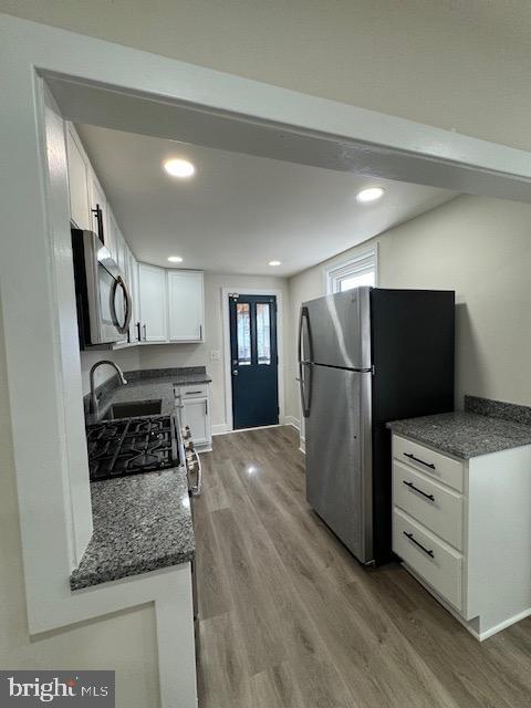 kitchen with recessed lighting, stainless steel appliances, a sink, wood finished floors, and white cabinets