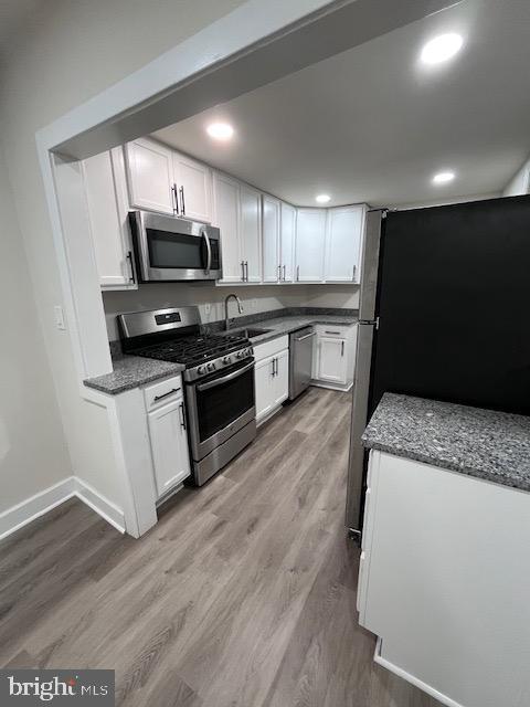 kitchen with stainless steel appliances, light wood-type flooring, a sink, and white cabinets