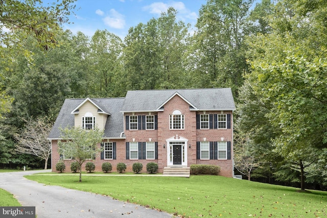 colonial house featuring brick siding, roof with shingles, and a front yard