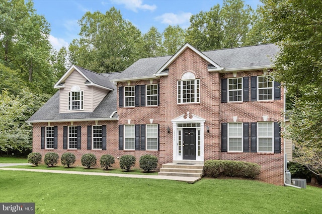 colonial inspired home featuring central air condition unit, brick siding, roof with shingles, and a front yard