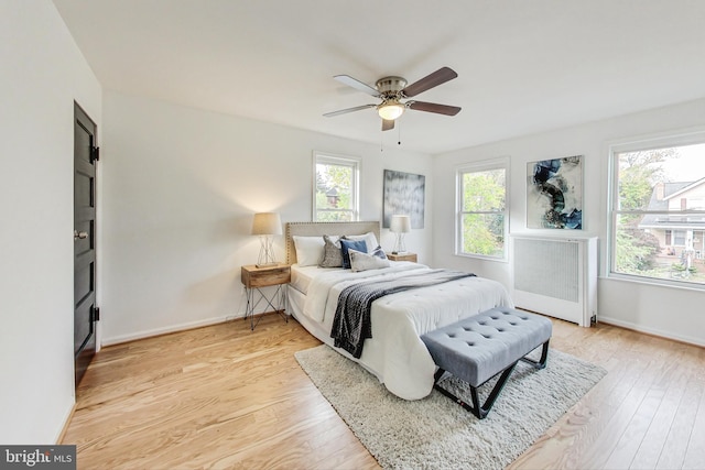 bedroom featuring radiator, multiple windows, light wood-type flooring, and ceiling fan