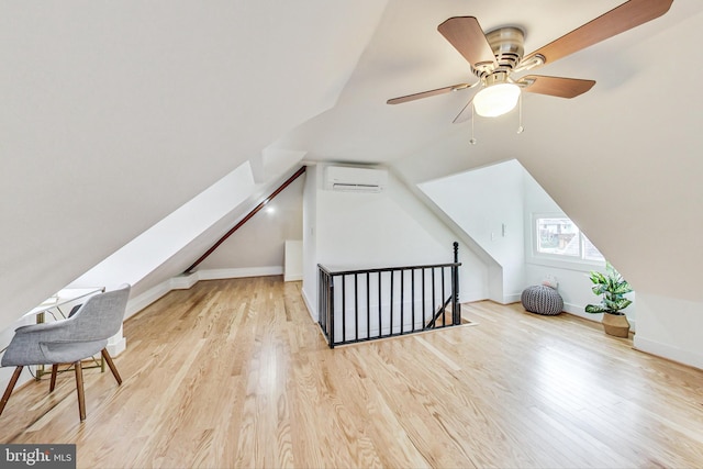 additional living space featuring lofted ceiling with skylight, a wall mounted AC, light hardwood / wood-style floors, and ceiling fan