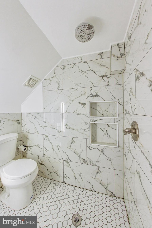 bathroom with toilet, tile patterned floors, tile walls, and tiled shower