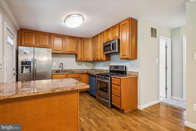 kitchen featuring light wood-type flooring, appliances with stainless steel finishes, light stone counters, and sink