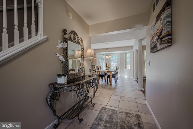 hallway featuring light tile patterned flooring, an inviting chandelier, and ornate columns