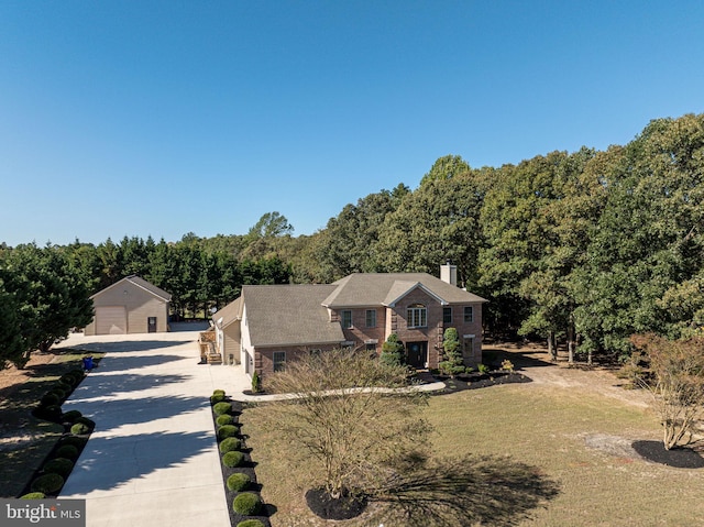 view of front facade with an outbuilding, a wooded view, a chimney, and a front yard