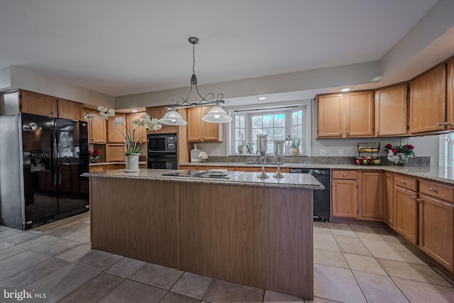 kitchen with light stone counters, black appliances, a center island, hanging light fixtures, and light tile patterned floors