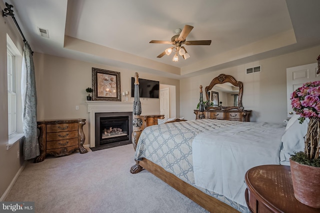 carpeted bedroom with ceiling fan and a raised ceiling