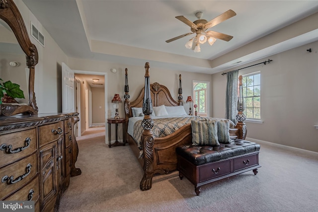 bedroom with a raised ceiling, light colored carpet, and ceiling fan