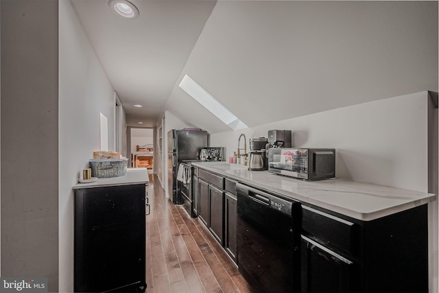 kitchen with lofted ceiling with skylight, sink, dishwasher, light stone countertops, and hardwood / wood-style flooring