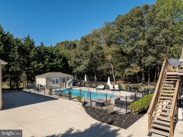 view of pool featuring an outbuilding, a water slide, and a patio area