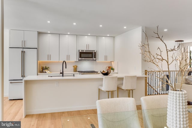 kitchen with white cabinets, stainless steel appliances, sink, and light hardwood / wood-style floors