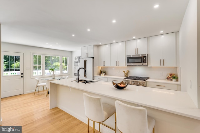 kitchen featuring light hardwood / wood-style flooring, stainless steel appliances, white cabinetry, sink, and a breakfast bar