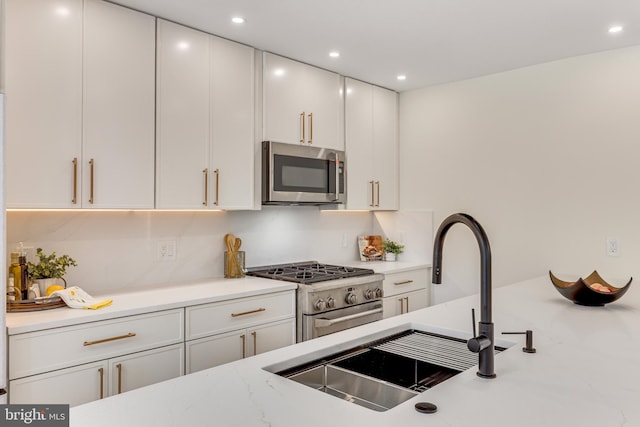 kitchen with light stone countertops, appliances with stainless steel finishes, sink, decorative backsplash, and white cabinetry