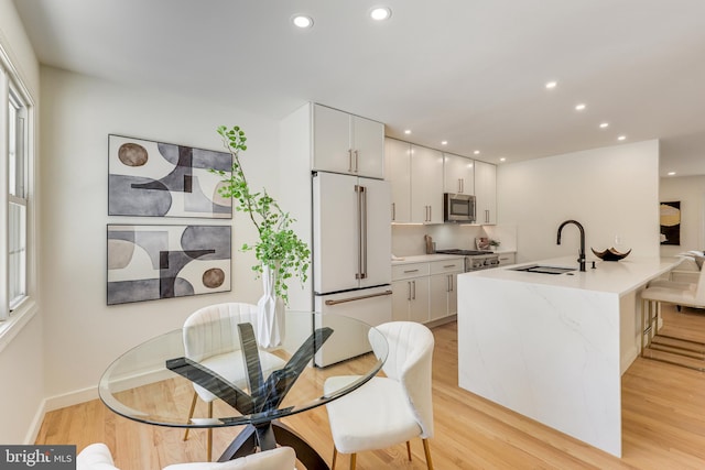 kitchen featuring light wood-type flooring, appliances with stainless steel finishes, white cabinetry, and sink