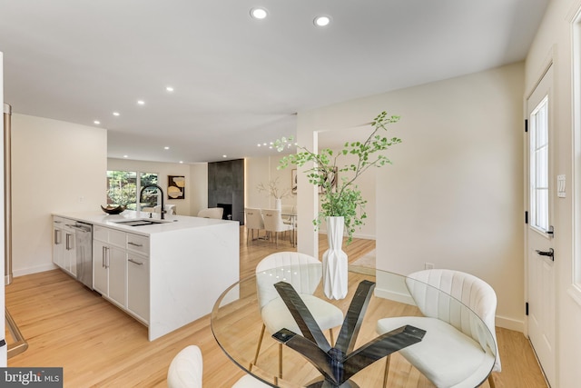 kitchen with a fireplace, light hardwood / wood-style flooring, dishwasher, sink, and white cabinets